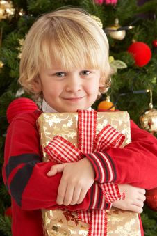 Young Boy Holding Gift In Front Of Christmas Tree Stock Image