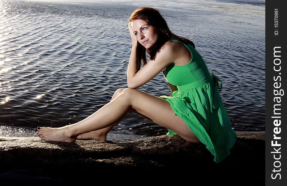 A beautiful young woman sitting on an islet in a green sundress. A beautiful young woman sitting on an islet in a green sundress.