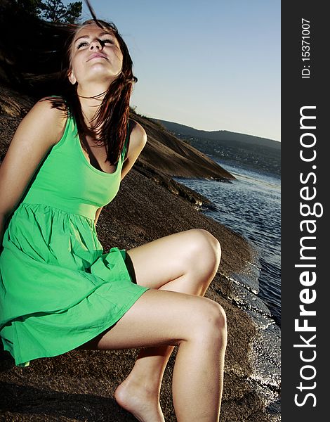 A beautiful young woman sitting on an islet in a green sundress throwing her hair back. A beautiful young woman sitting on an islet in a green sundress throwing her hair back