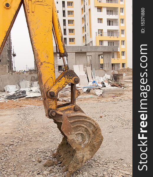 Arm and bucket of a digger in front of a building under construction. Arm and bucket of a digger in front of a building under construction