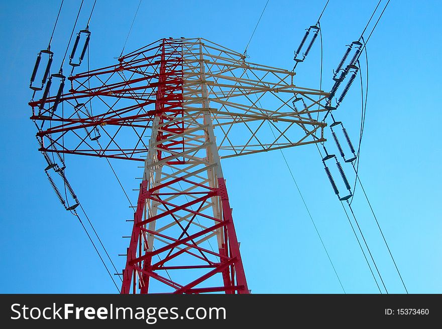 Top of the red and white high voltage electricity pylon against the blue sky. Top of the red and white high voltage electricity pylon against the blue sky