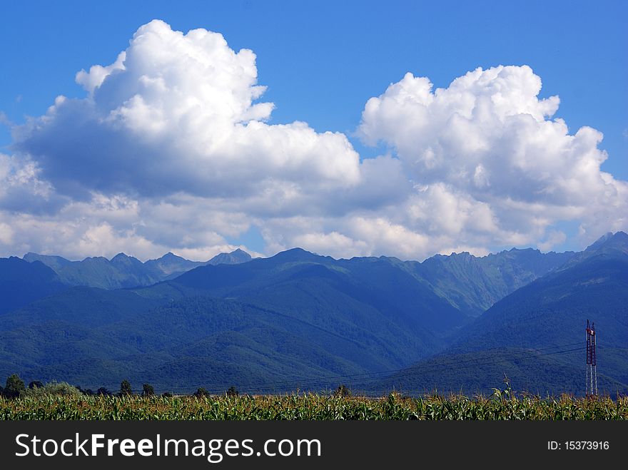 Beautiful landscape with fluffy clouds over far mountains near sunny meadow