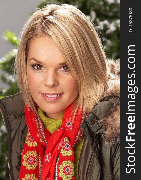 Fashionable Woman Wearing Parka Coat And Scarf In Studio In Front Of Christmas Tree