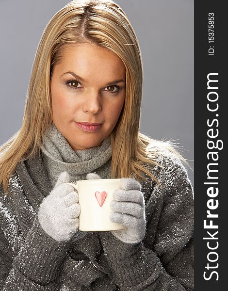 Young Woman Drinking Hot Drink Wearing Knitwear In Studio In Front Of Christmas Tree