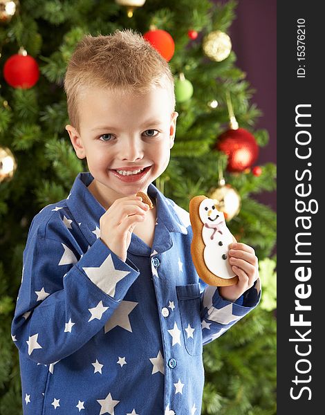 Young Boy Eating Cookie In Front Of Christmas Tree Smiling