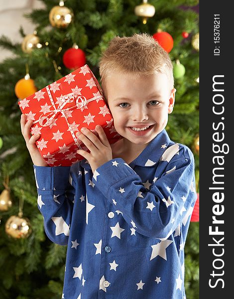 Young Boy Holding Wrapped Present In Front Of Christmas Tree. Young Boy Holding Wrapped Present In Front Of Christmas Tree