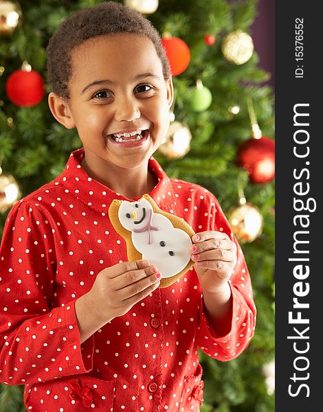 Young Boy Eating Cookie In Front Of Christmas Tree