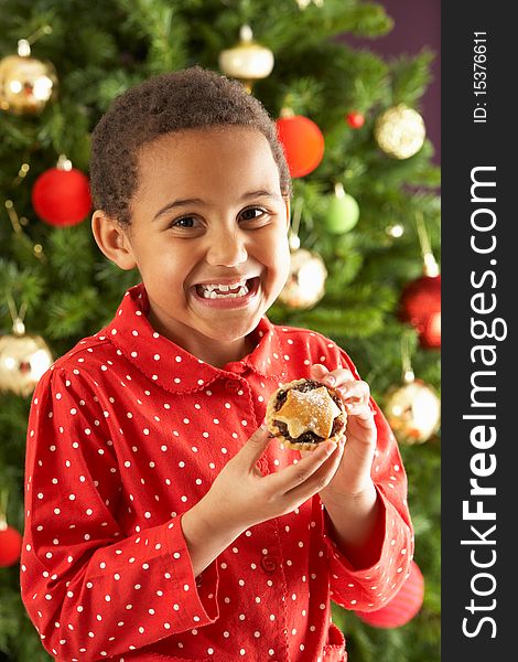 Boy Eating Mince Pie In Front Of Christmas Tree