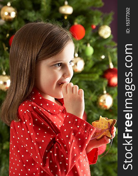 Young Girl Eating Star Shaped Christmas Cookie In Front Of Christmas Tree. Young Girl Eating Star Shaped Christmas Cookie In Front Of Christmas Tree