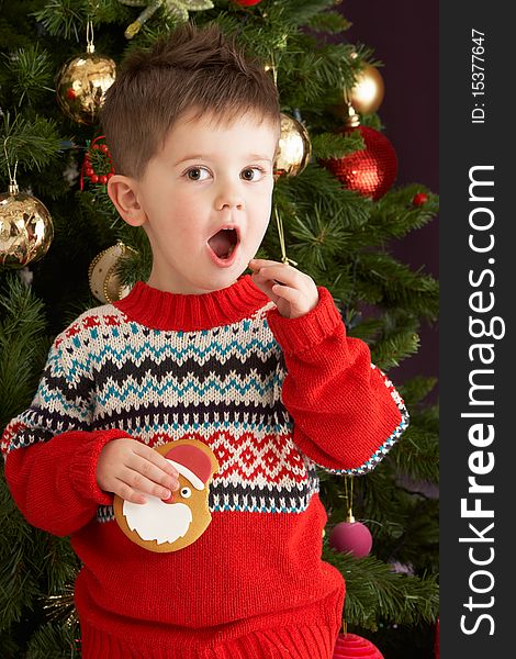 Boy Eating Cookie In Front Of Christmas Tree