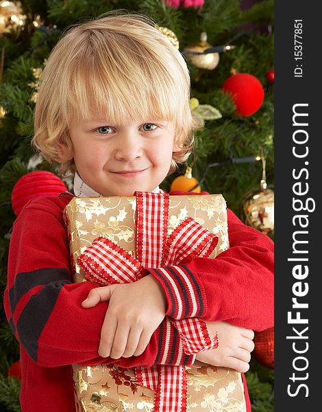 Young Boy Holding Gift In Front Of Christmas Tree