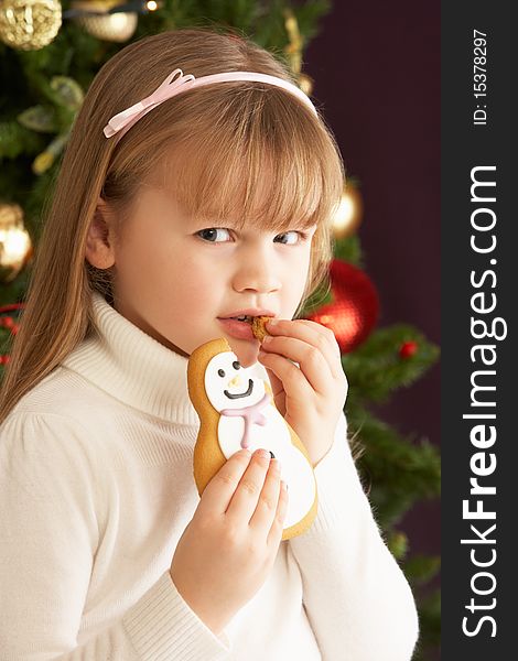 Young Girl Eating Cookie In Front Of Christmas Tree