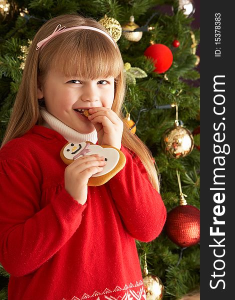 Young Girl Eating Cookie In Front Of Christmas Tree