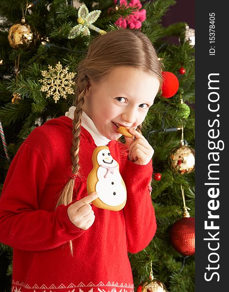 Young Girl Eating Cookie In Front Of Christmas Tree