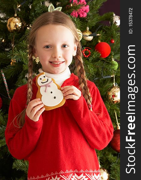 Young Girl Eating Cookie In Front Of Christmas Tree