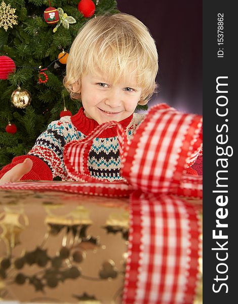 Boy Holding Gift In Front Of Christmas Tree