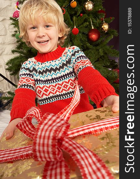 Young Boy Holding Gift In Front Of Christmas Tree Smiling