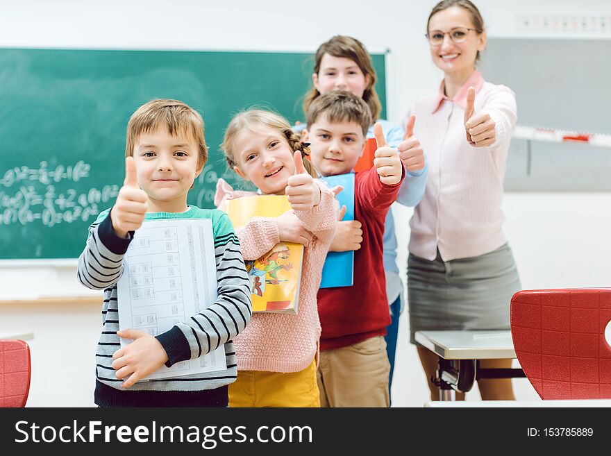 Pupils and teacher showing thumbs-up in school having fun in class