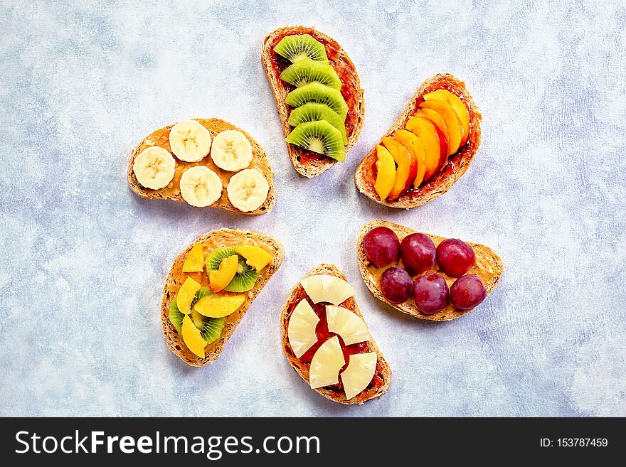 Healthy breakfast toasts with peanut butter, strawberry jam, banana, grapes, peach, kiwi, pineapple, nuts. Copy space