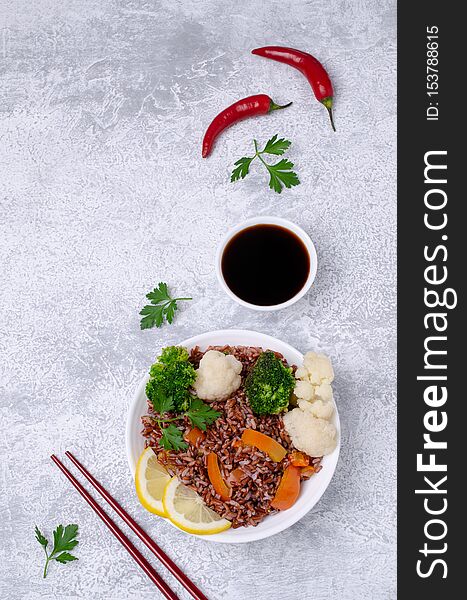 Unpolished red rice with vegetables in a ceramic dish on a slate background. Selective focus