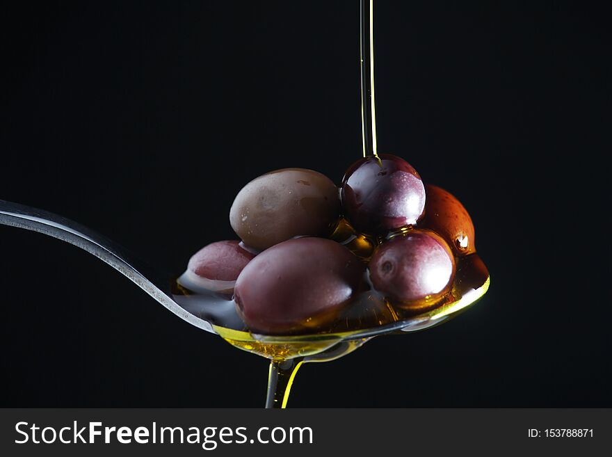 A spoon full of black olives  at dark background