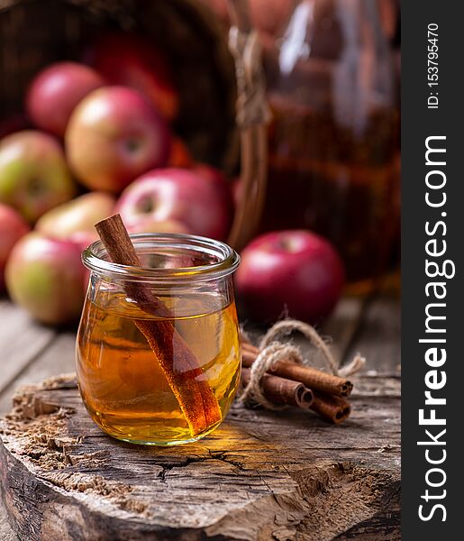 Glass of apple cider with cinnamon sticks on a rustic wood surface with red apples in background