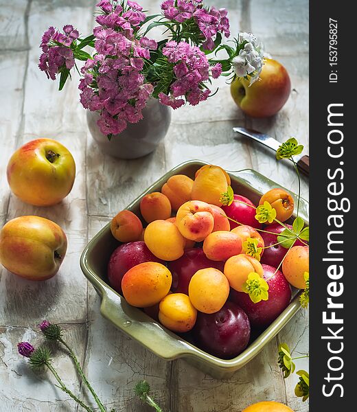 Fruit set of fresh fruits in a ceramic plate, a bouquet of forest carnations in a small vase