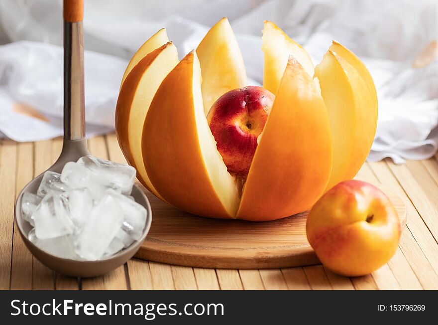 Ripe yellow melon cut into slices in the form of a flower stuffed with whole nectarine is on the kitchen table. Ladle with ice