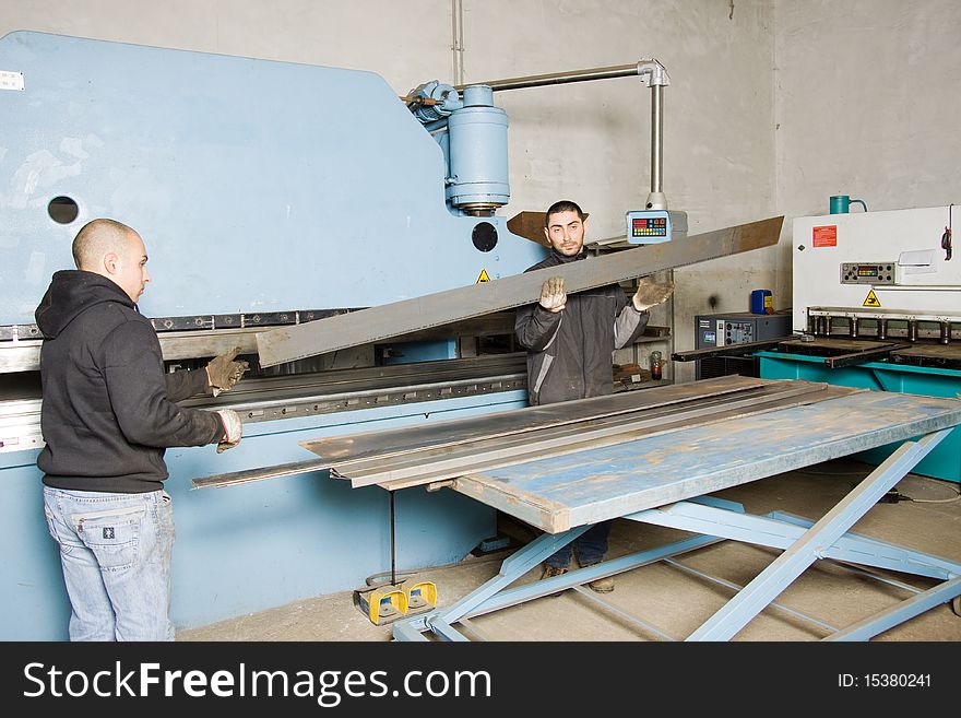 Metalworkers at work in their workshop forging the iron with a machine. Metalworkers at work in their workshop forging the iron with a machine