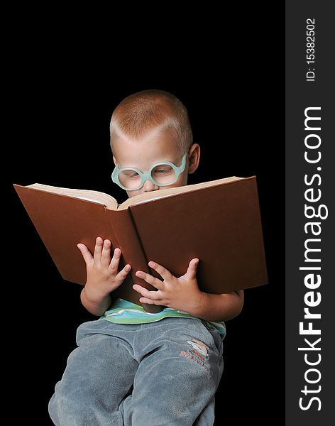 Cute boy with glasses reading a big book isolated on a black background. Cute boy with glasses reading a big book isolated on a black background