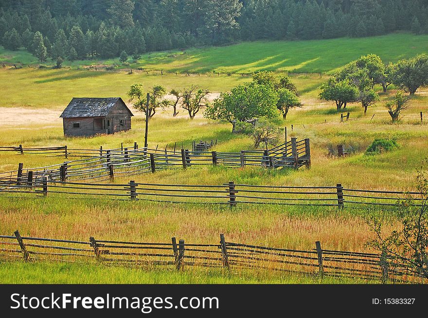 Old wooden shack in lush green meadow with wooden fences. Old wooden shack in lush green meadow with wooden fences