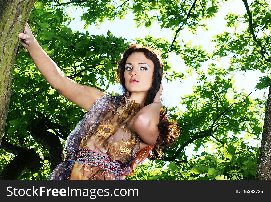 Fashion shoot of a young brunette girl in a light colorful dress. The image is taken outdoors, on a nature background with trees. Fashion shoot of a young brunette girl in a light colorful dress. The image is taken outdoors, on a nature background with trees.