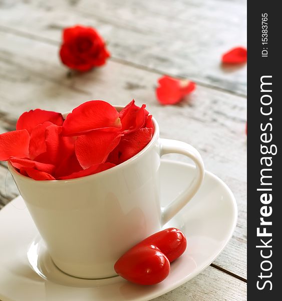 Cup of red rose petals and red heart on old wooden board