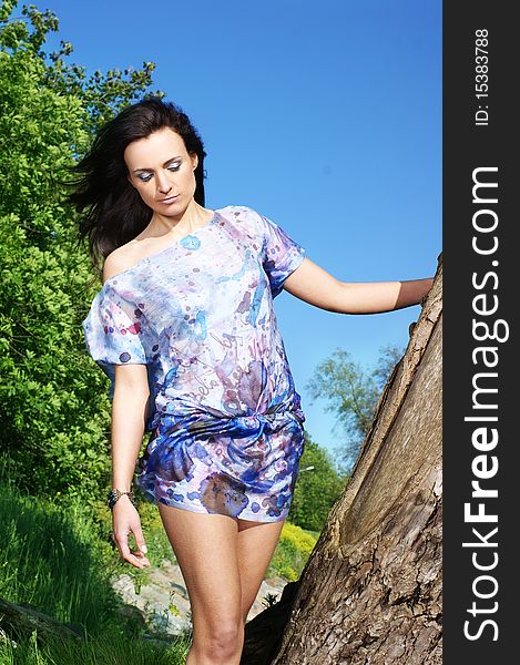 Fashion shoot of a young brunette girl in a light colorful dress. The image is taken outdoors, on a nature background with trees and water. Fashion shoot of a young brunette girl in a light colorful dress. The image is taken outdoors, on a nature background with trees and water.