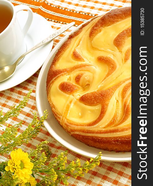 Appetizing cake, cup of tea and flowers on checkered tablecloth
