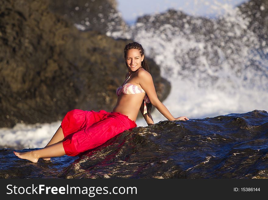 Young beautiful tanned girl sitting on rocks