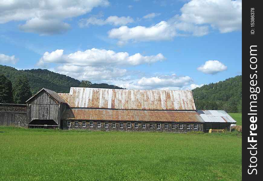 A long barn sits in a field in a valley in Vermont with the mountains in the background. A long barn sits in a field in a valley in Vermont with the mountains in the background.