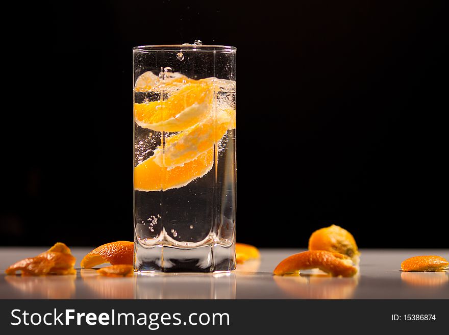 Pieces of orange floating in a glass of water on black background. On the bottom there are pieces of orange peel. Pieces of orange floating in a glass of water on black background. On the bottom there are pieces of orange peel.