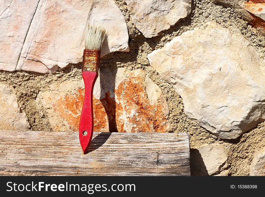 Old red paint brush drying on piece of wood, leaning on stone wall in the sunlight. Old red paint brush drying on piece of wood, leaning on stone wall in the sunlight