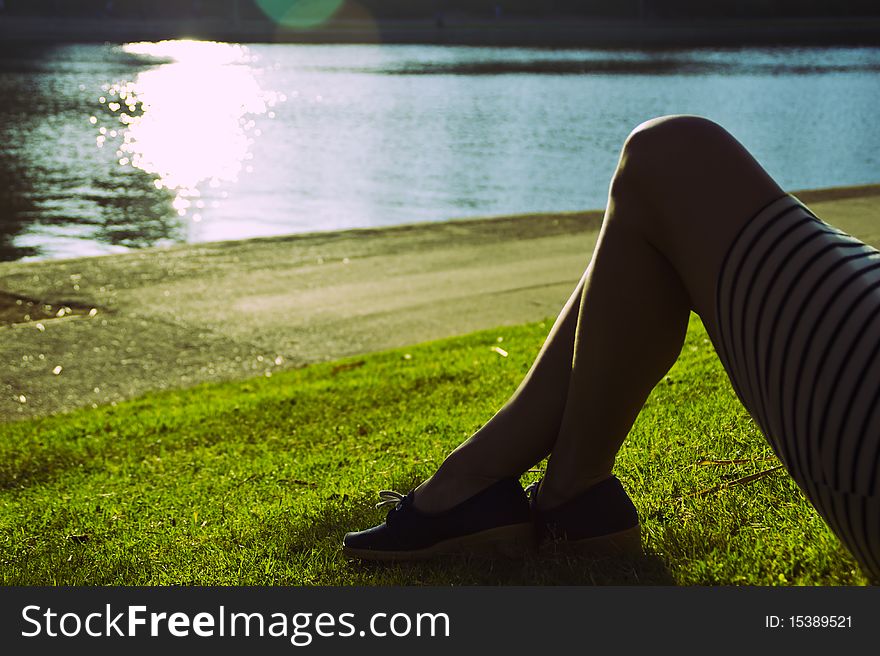 A woman's legs as she sits in the grass by water. A woman's legs as she sits in the grass by water.