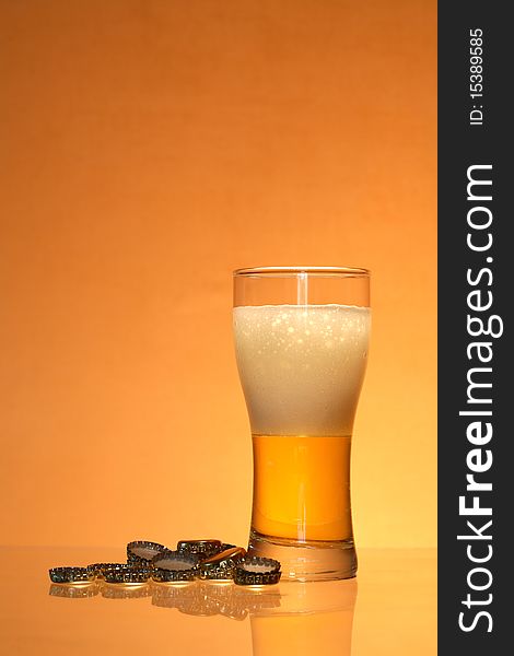 Bottle caps lying near glass of light beer with foam