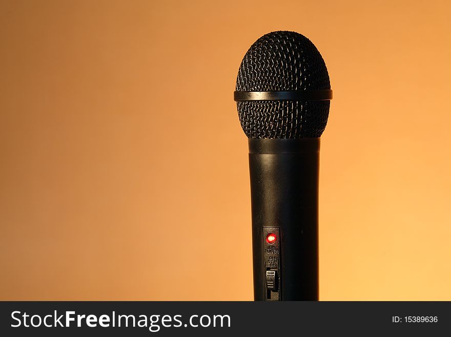 A modern black handheld ball head microphone on ginger background with copy space. A modern black handheld ball head microphone on ginger background with copy space