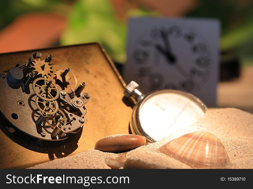 Abstract background with old clock mechanism standing on sand with stones and shells. Abstract background with old clock mechanism standing on sand with stones and shells