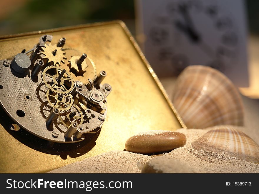 Abstract background with old clock mechanism standing on sand with stones and shells. Abstract background with old clock mechanism standing on sand with stones and shells