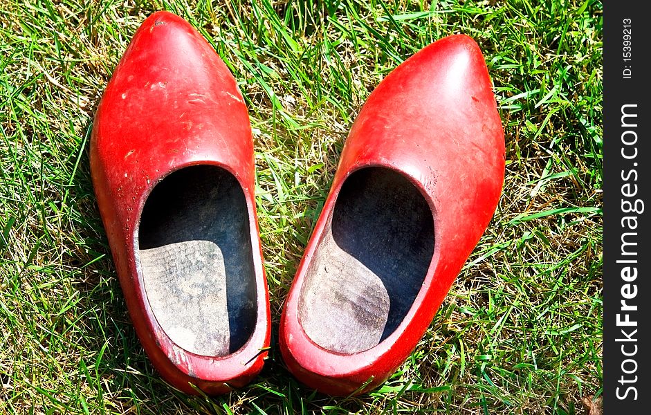 A pair of old, red, wooden shoes in the grass. A pair of old, red, wooden shoes in the grass.