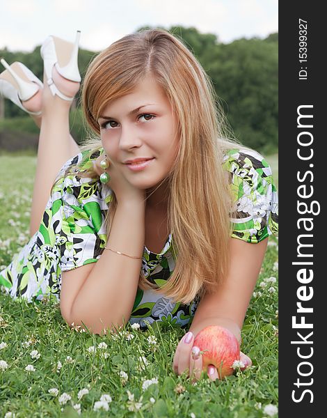 Young beautiful girl relaxing on the field with an apple in his hand. Young beautiful girl relaxing on the field with an apple in his hand