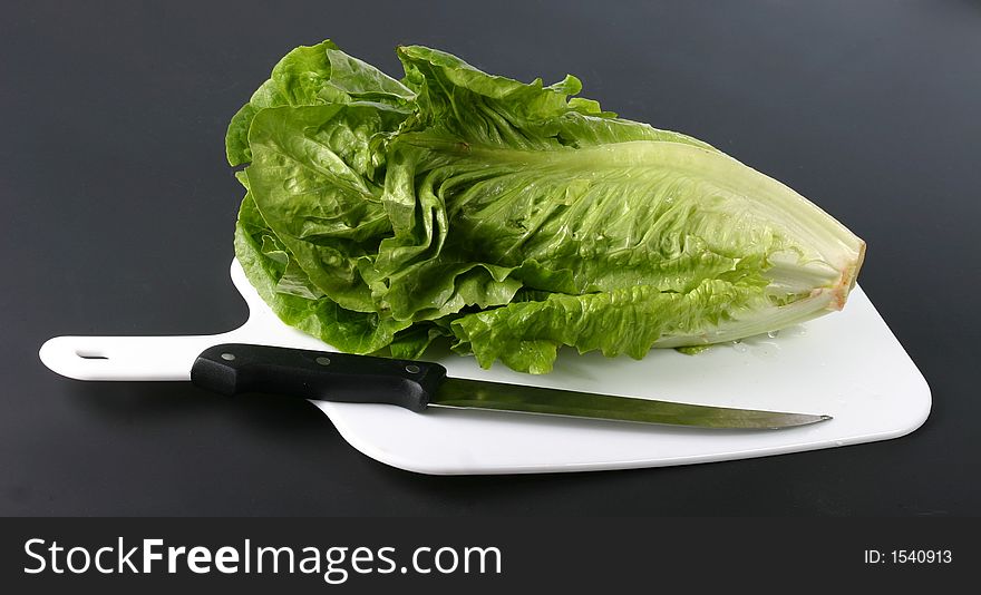 Green lettuce on cutting board with knife on a black background