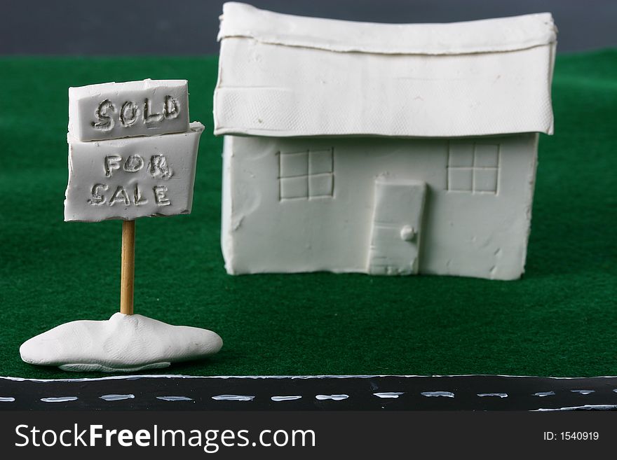 A whimsical clay house with a for sale sign and a sold sign. A whimsical clay house with a for sale sign and a sold sign