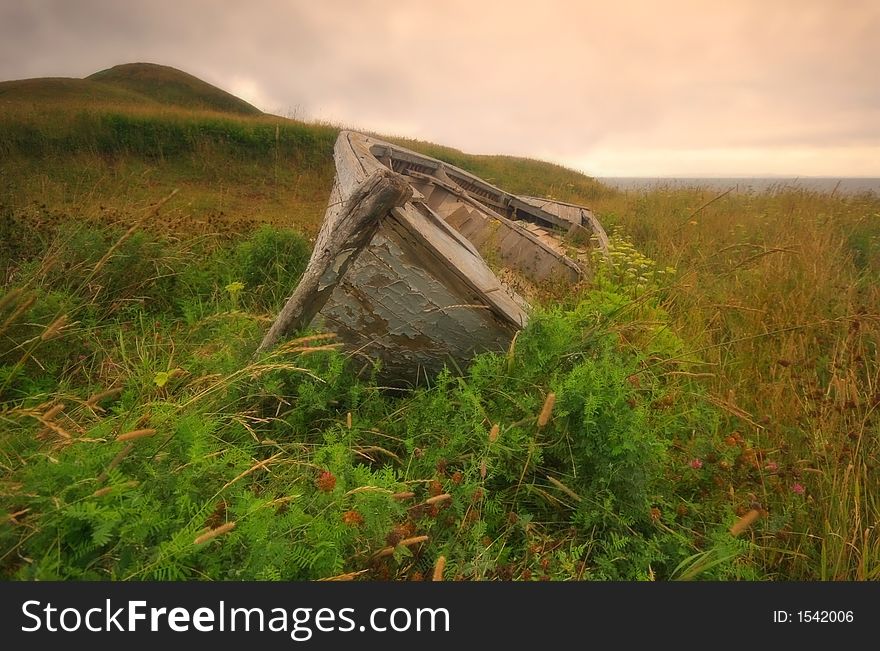 An old, abandoned wooden boat left in grass near La Grave, Iles de madeleine, Quebec. An old, abandoned wooden boat left in grass near La Grave, Iles de madeleine, Quebec