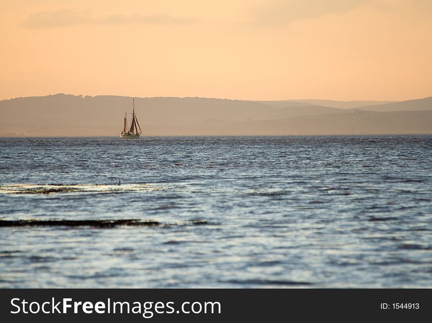 Sailing ship in the Bristol Channel as the sun goes down and bathes the scene in orange light. Sailing ship in the Bristol Channel as the sun goes down and bathes the scene in orange light